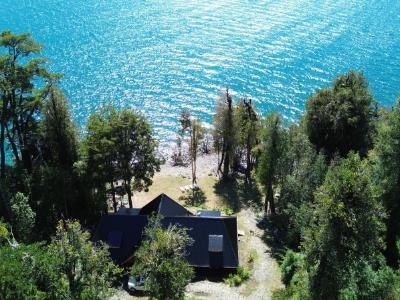 Aerial view of the house with a black roof, nestled in trees near the turquoise water.